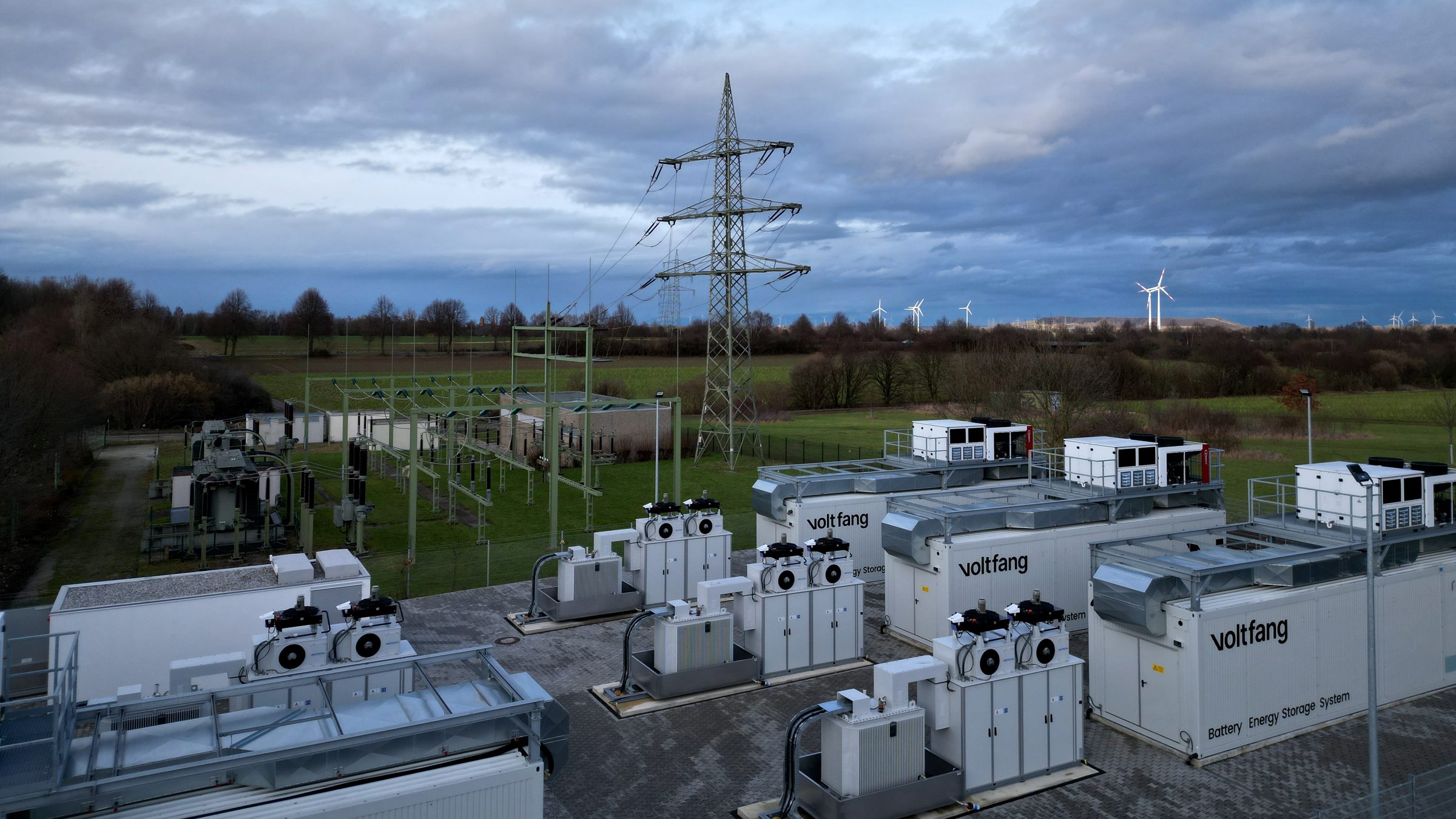 Großbatteriespeicher von Voltfang in Alsdorf mit Umspannwerk, Strommast und Windrädern im Hintergrund, aus der Luft fotografiert